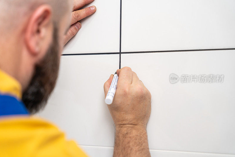 一名男子用黑色丙烯酸记号笔在浴室的瓷砖接缝处涂上白色浆液