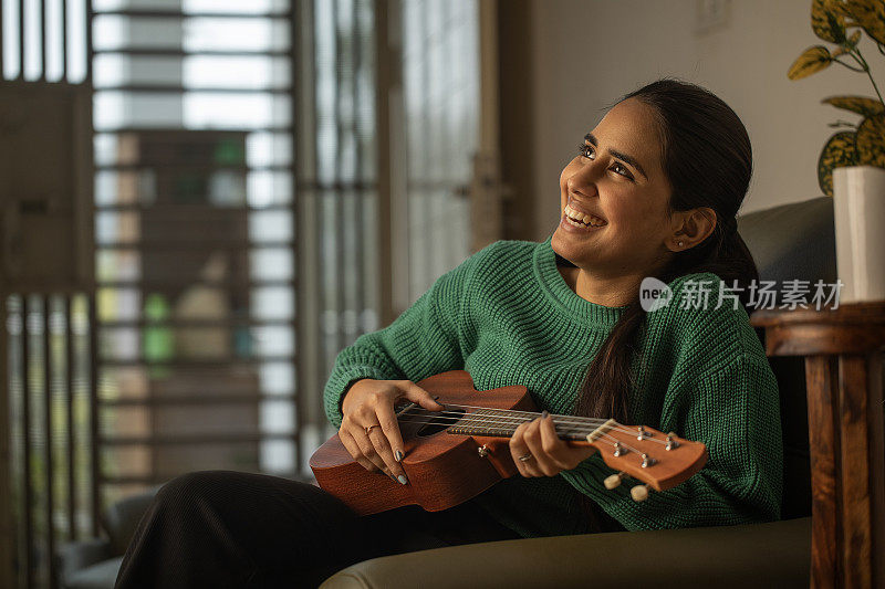 快乐的女人在家里的沙发上弹吉他