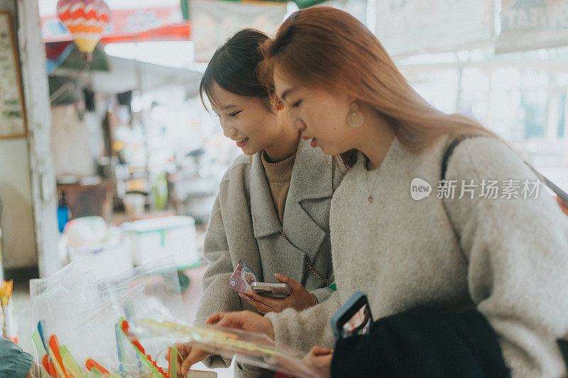 两个年轻的亚洲妇女在香港市场浏览商品。