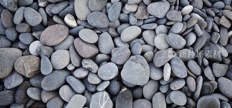 光滑的圆形鹅卵石纹理背景。卵石海沙滩特写，深色湿卵石和灰色干卵石。高质量照片