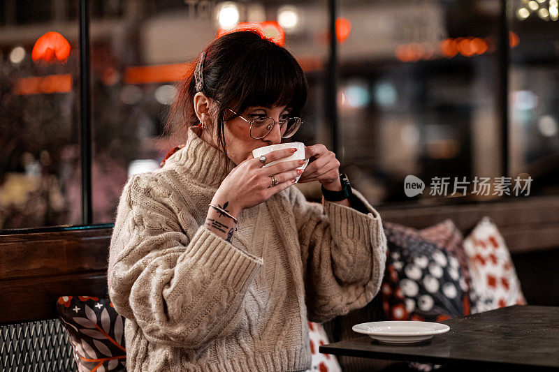 在餐馆里喝咖啡的女人。她穿着一件高领毛衣，戴着一副眼镜