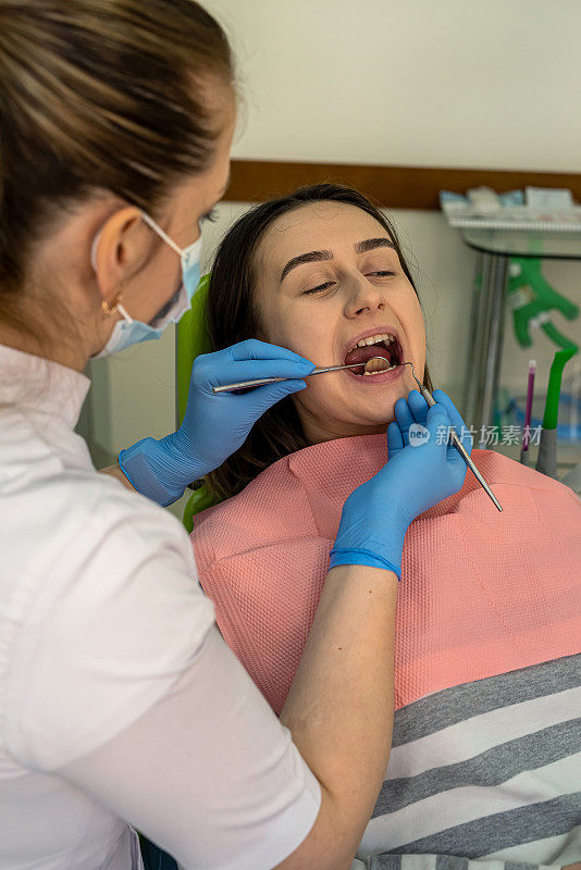 女牙医在牙科诊所用牙科仪器检查年轻女病人的牙齿