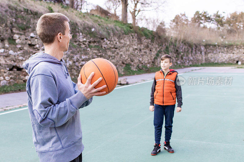 父亲和儿子在球场上打篮球，教小球员。幸福和健康的家庭快乐。户外运动。