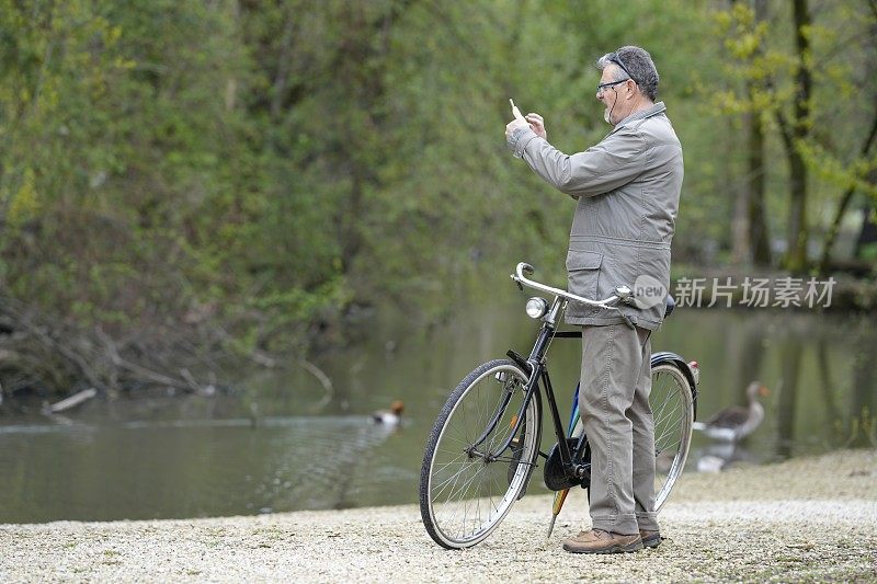 一名男子在池塘前用智能手机拍照