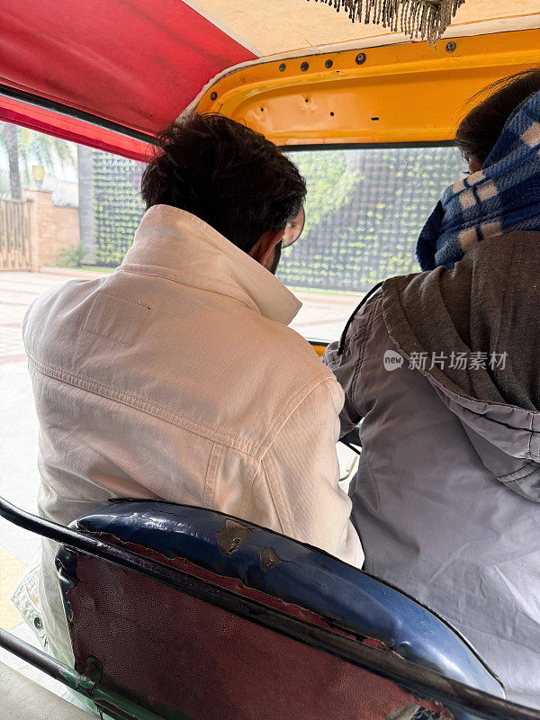 乘客坐在三轮车司机旁边的特写图像，后视图，焦点在前景
