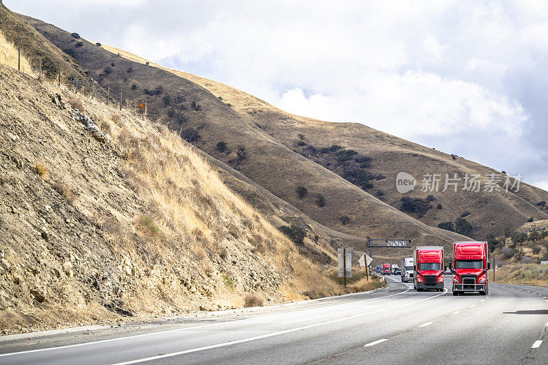 两辆红色大钻机半挂车组成的车队，用干式货车半挂车运输货物，在加利福尼亚州的山区公路上坡行驶