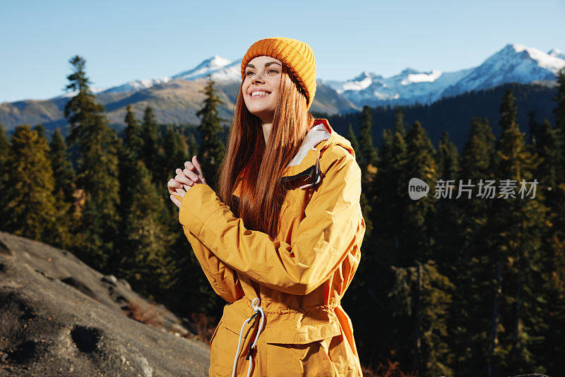 女人笑着笑着幸福和笑声旅游者穿着黄色的雨衣在秋天旅行，在日落的阳光下在山上徒步旅行自由