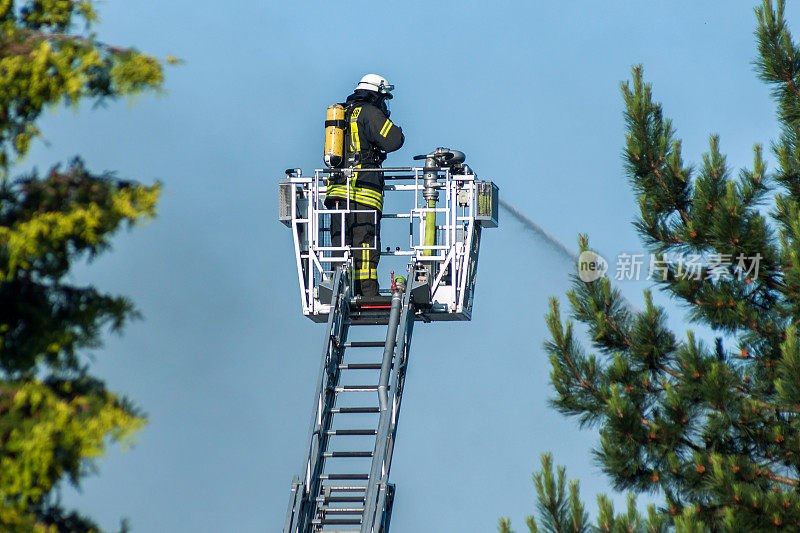 戴头盔的消防队员在大梯子上灭火