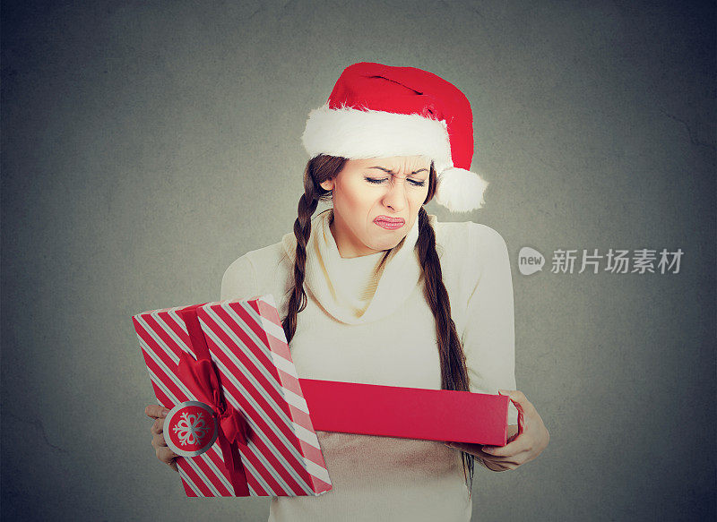 年轻女子戴着红色的圣诞老人帽子打开礼物，收到的东西让她非常难过