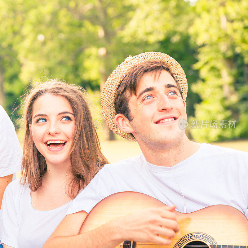 年轻夫妇在树下和阳光下弹吉他唱歌