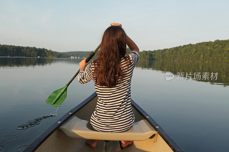 年轻女孩在平静的湖面上划着独木舟