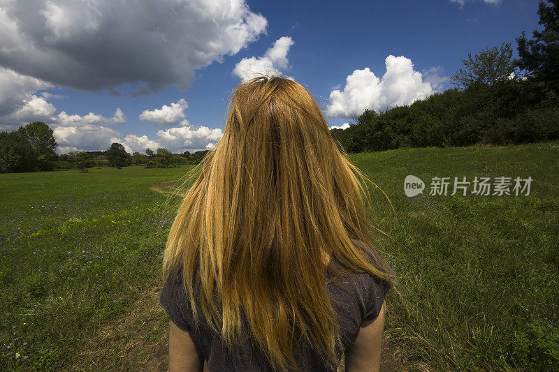 金发女孩在大自然中漫步，风吹着她的头发