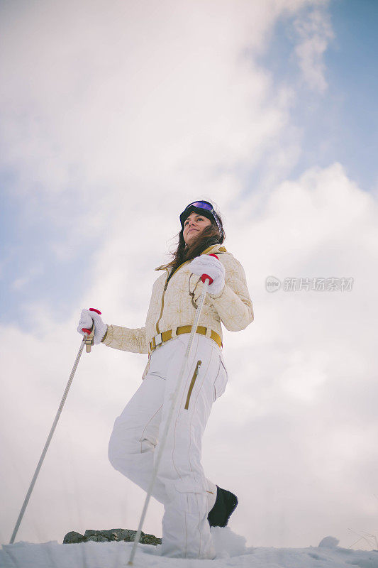 近景美丽的年轻女子在冬天的衣服站在一边，手拿木棍的背景雪山