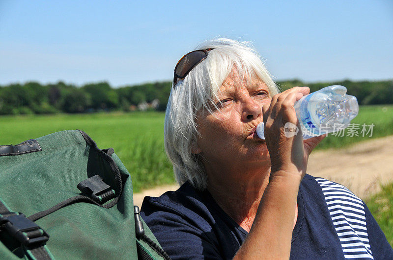 在户外喝瓶装水的老妇人