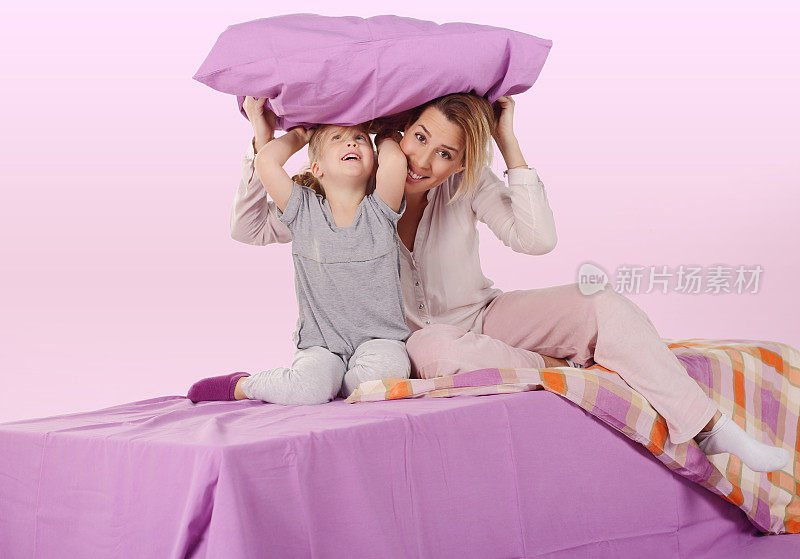 可爱的女孩和她的妈妈在床上抱着紫色的枕头