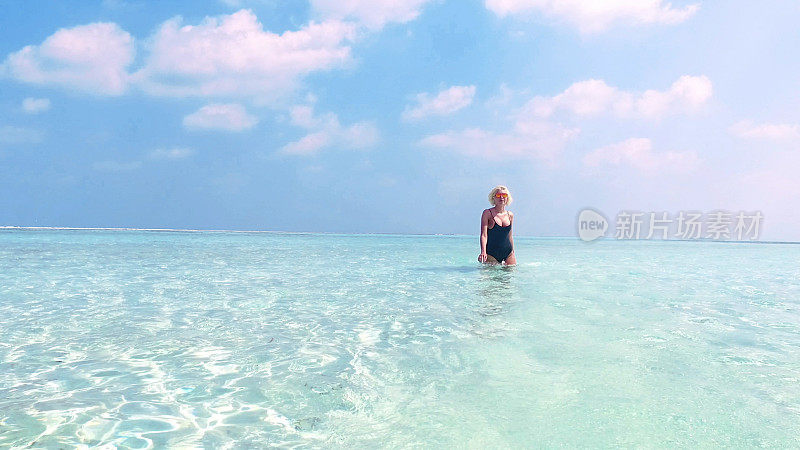性感的金发女人走过马尔代夫的浅水