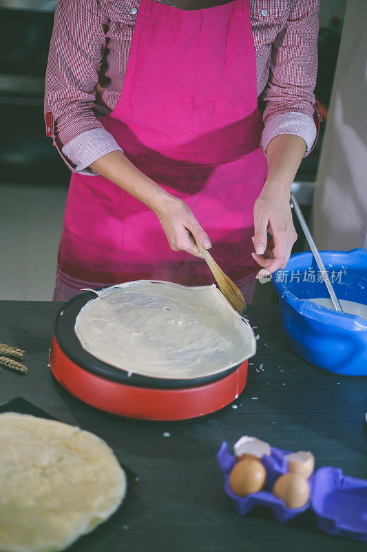 女孩倒了一勺面团做煎饼。在家做煎饼。