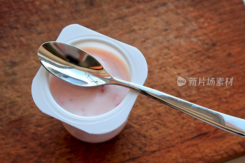 粉红色的酸奶在塑料杯和勺子的木制背景。