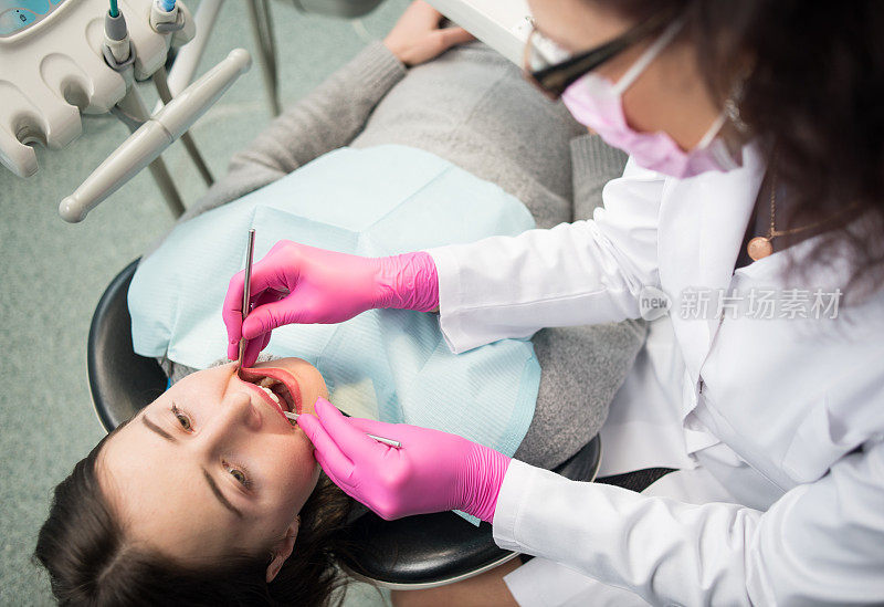 年轻女子正在牙科诊所进行牙科检查。牙医用牙科工具-镜子和探针检查病人的牙齿。牙医。