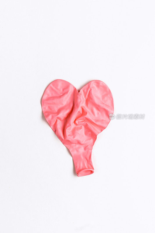 瘪了的皱巴巴的粉红色心形气球平躺在白色的背景上