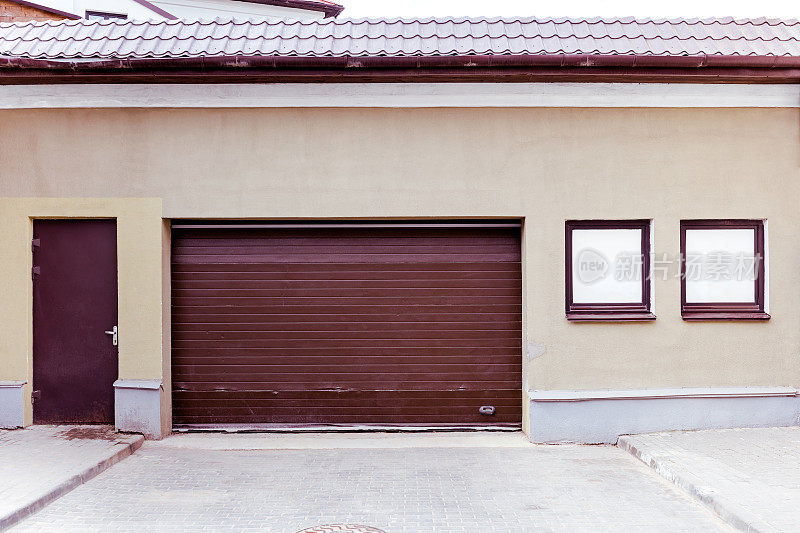 封闭的棕色波纹金属车库门与门口和窗户在石膏墙上