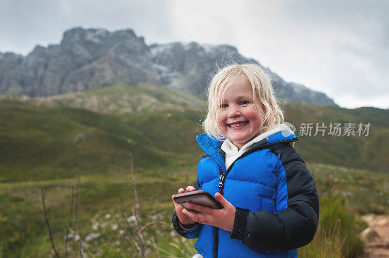 非常快乐的蹒跚学步的女孩玩智能手机在自然