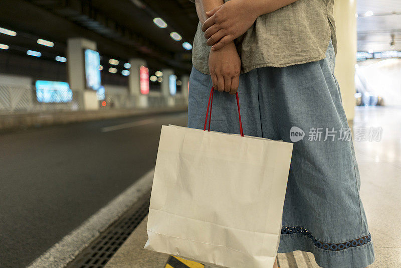 女孩拿着购物袋，在路边等车