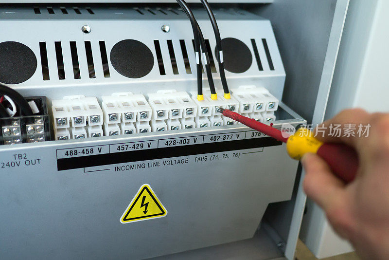电工手用螺丝刀拧紧电气柜内变压器的电气端子