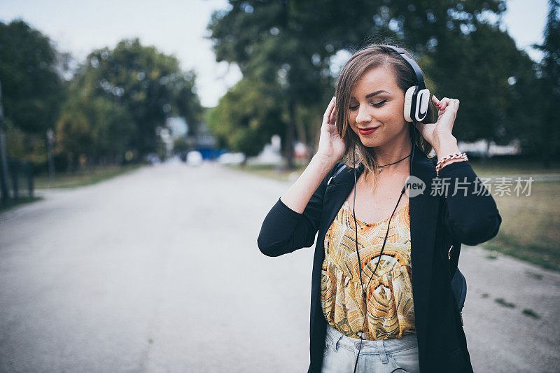 美丽的女人戴着耳机在公园里听音乐