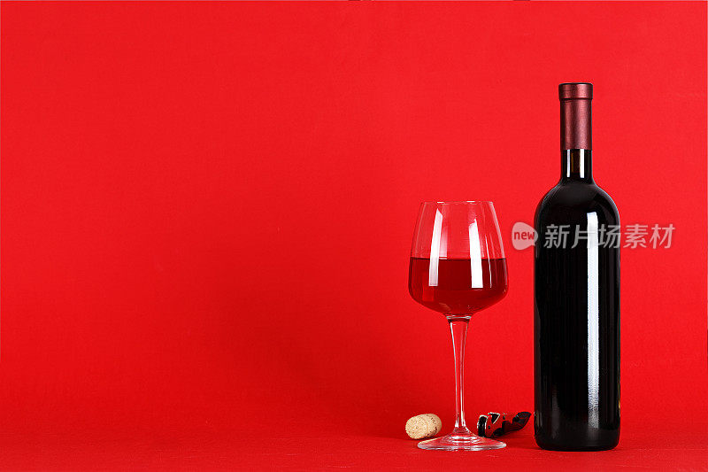 红酒置于红色背景上-一瓶红酒与一只盛满酒的酒杯置于红色背景上