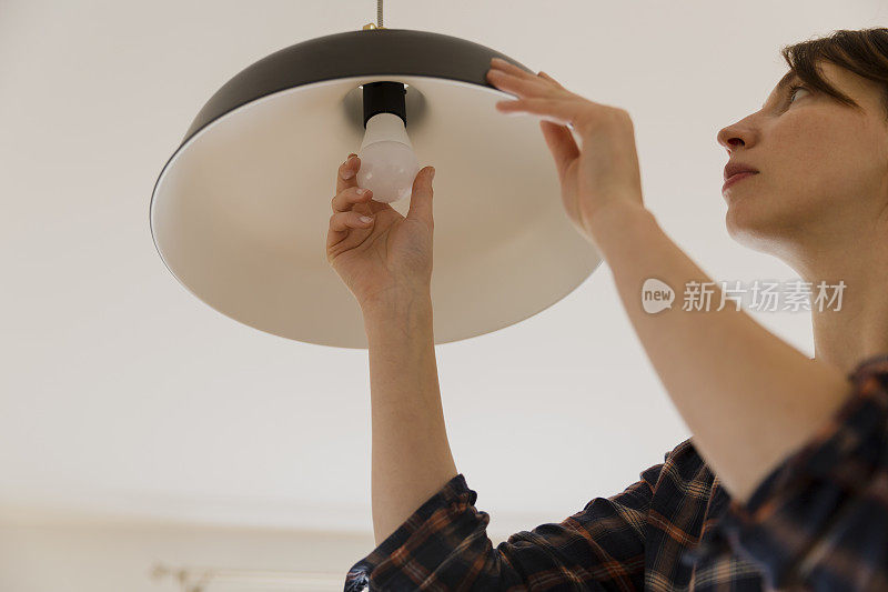 妇女在家里更换灯泡。节能LED灯更换