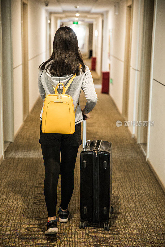 一个女人拿着行李走在酒店的走廊上