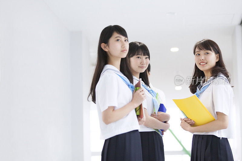 三个女孩微笑着拿着笔记本在学校走廊里
