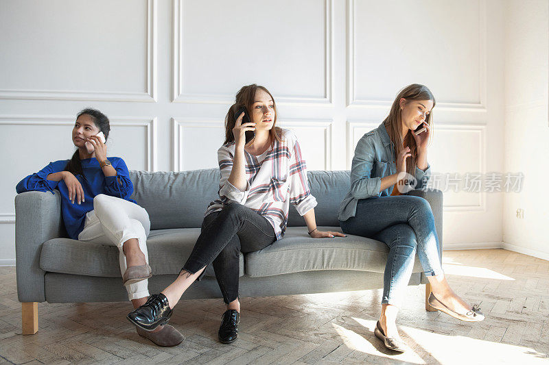 三个年轻女人在沙发上拿着手机