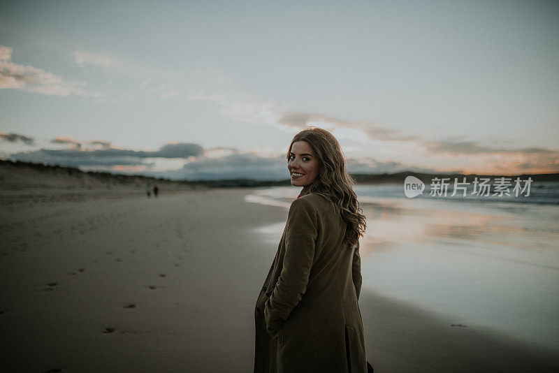 一个年轻女子在冬天的夕阳下走过海滩