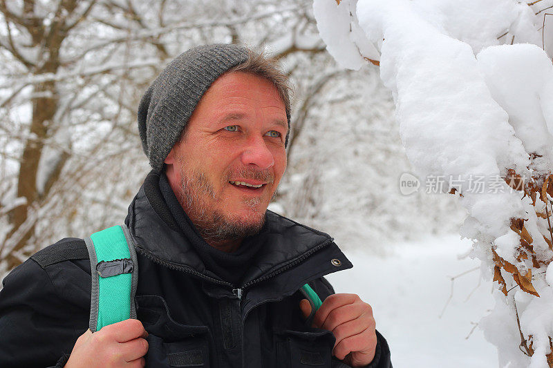 美丽微笑的成年男子徒步旅行者戴着针织帽徒步雪山森林的肖像