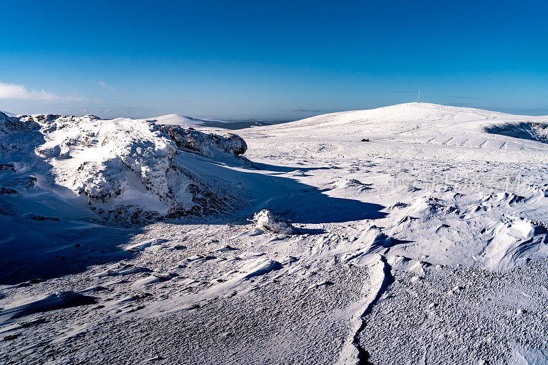 野生景观覆盖在积雪的冬天，岩石的前景，遥远的山脉和蓝天