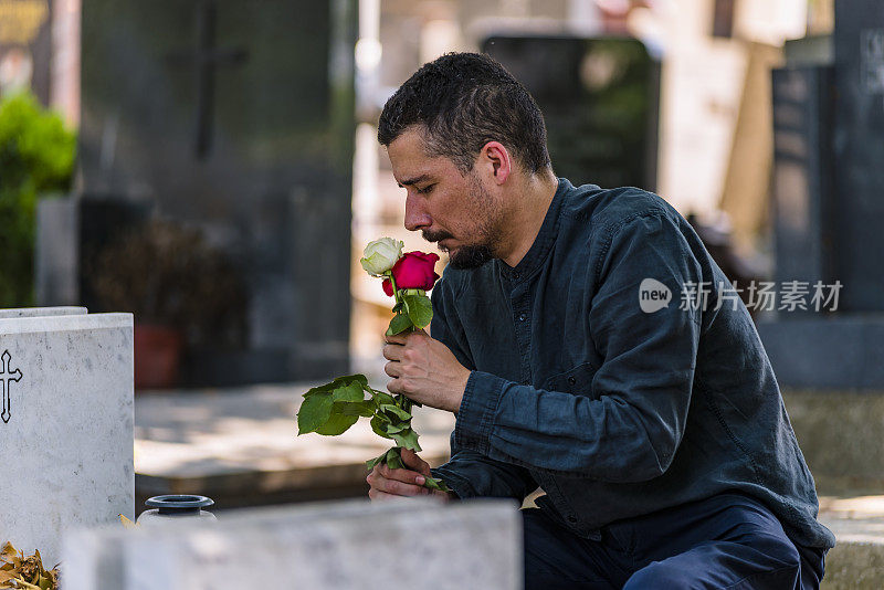 悲伤中的男性鳏夫与玫瑰花束在墓地