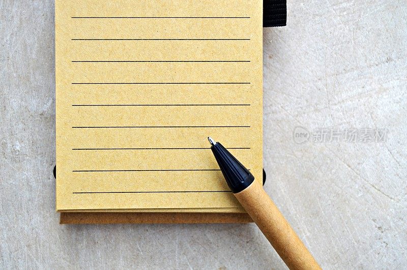 一个单行空白的黄色米黄色记事本页和棕色和黑色钢笔放在上面，在一个木制的米黄色邋遢的复古水平背景。