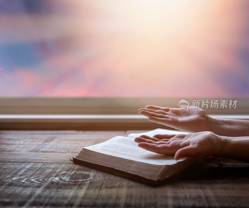 在崇拜中，女人举起双手，用戏剧性的光阅读《圣经》。木头桌子，阳光从窗户射进来。基督教的形象