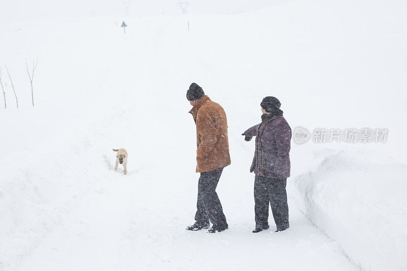 一对老年夫妇在下雪的乡村路上穿着暖和的衣服