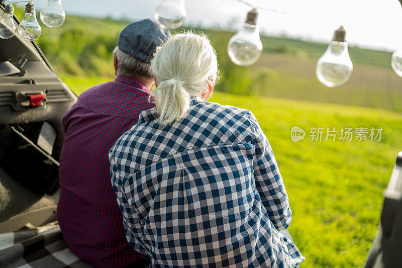 一对快乐的老夫妇坐在他们的汽车后备箱里