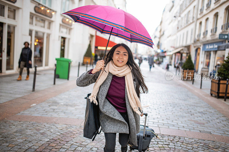亚洲游客拿着旅行箱和雨伞在城市里散步