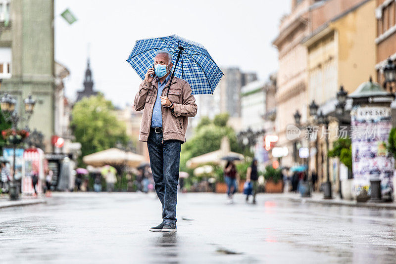 一个随意的老人在雨天走在城市里打电话。