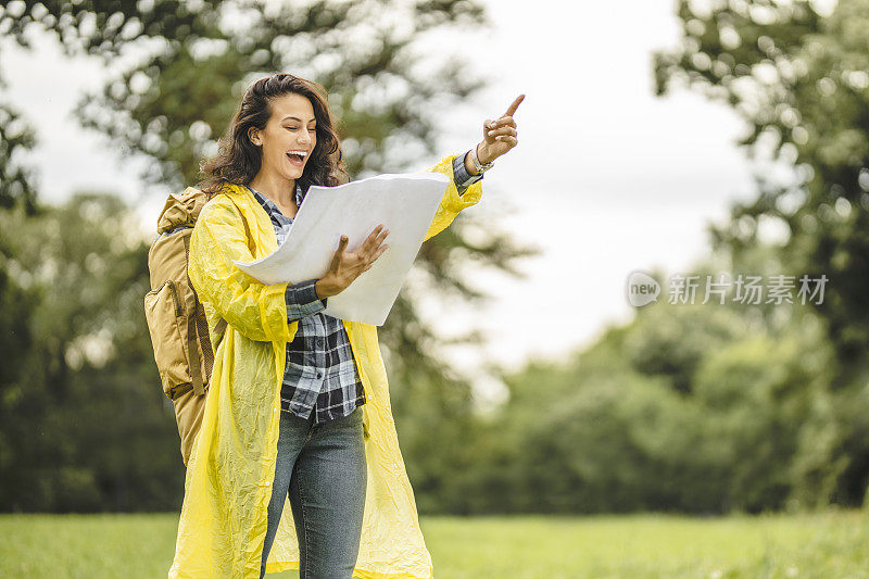 年轻女子穿着防水夹克，看地图，在雨中徒步旅行