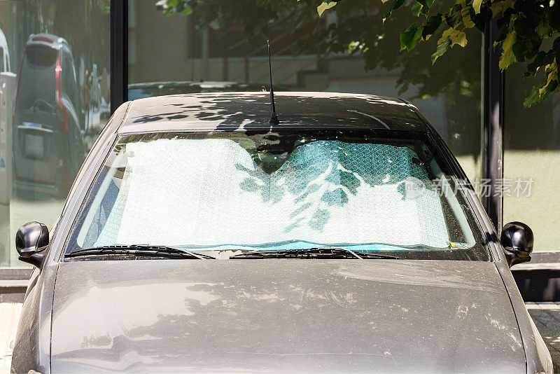 在户外停了一天的灰色汽车挡风玻璃下的遮阳板可以保护它不被太阳晒伤。金属银箔制成的箔式遮阳板可以直接反射阳光。