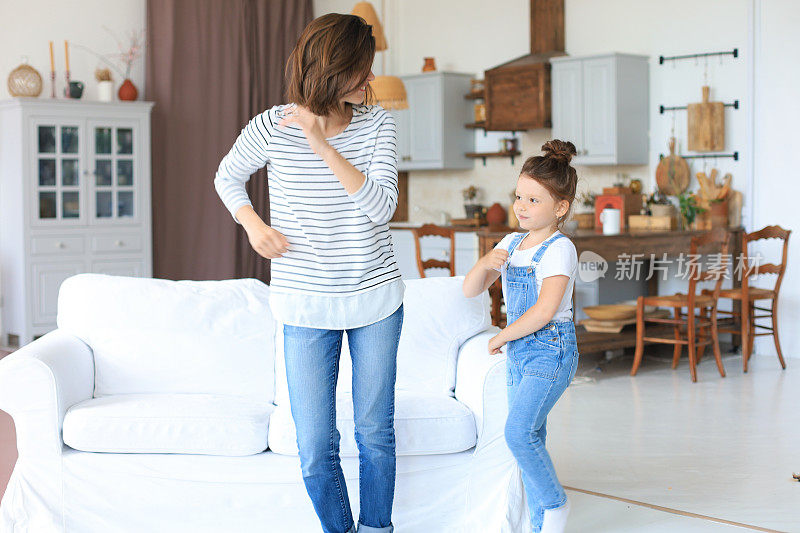 快乐的母亲和小女儿在家里的客厅里唱着最喜欢的歌跳舞。