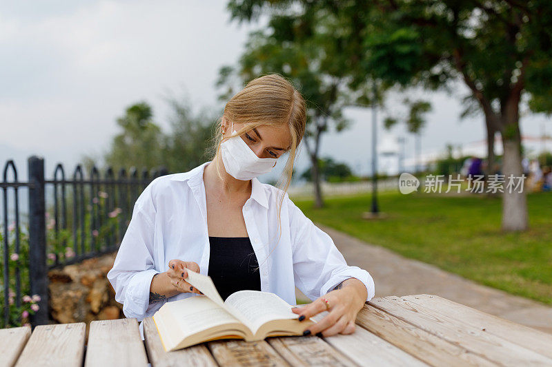 年轻妇女戴着防护口罩在公园看书(模拟读书人)