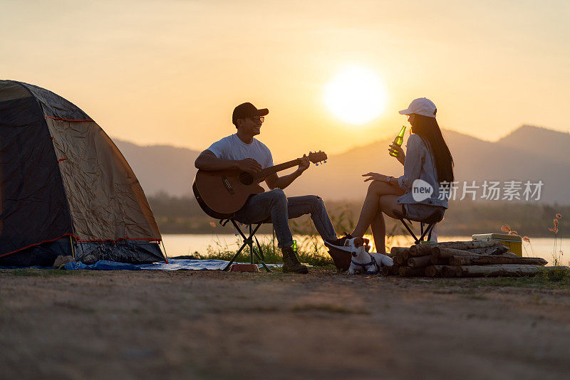 亚洲夫妇与狗弹吉他和喝啤酒旁边的帐篷营地