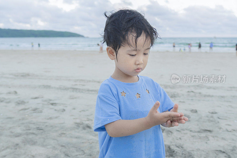 黄昏时分，一个可爱的亚洲小女孩在沙滩上玩完沙子和水后正在清理她的双手